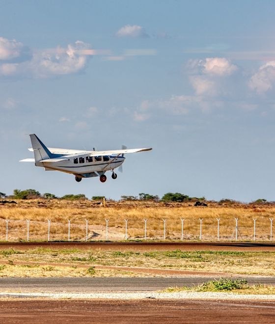 A small plane taking off from an airstrip with mountains in the background.